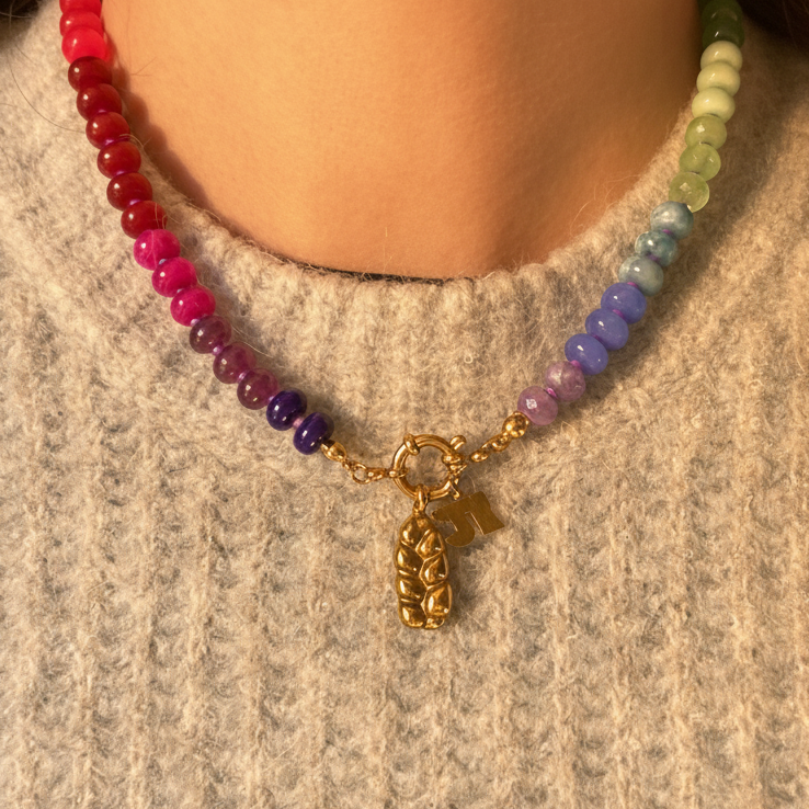 Colorful beaded necklace with a gold charm on a person wearing a gray sweater.