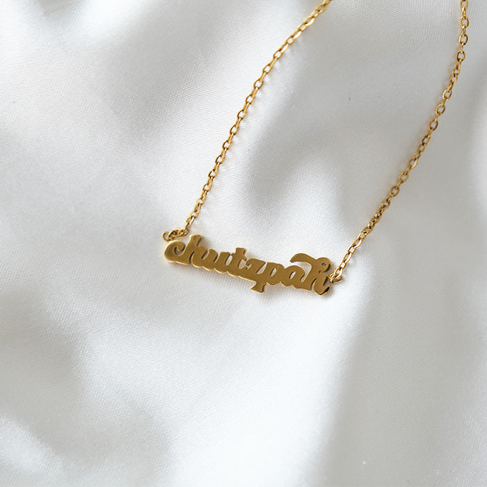 Gold chutzpah necklace on white fabric.