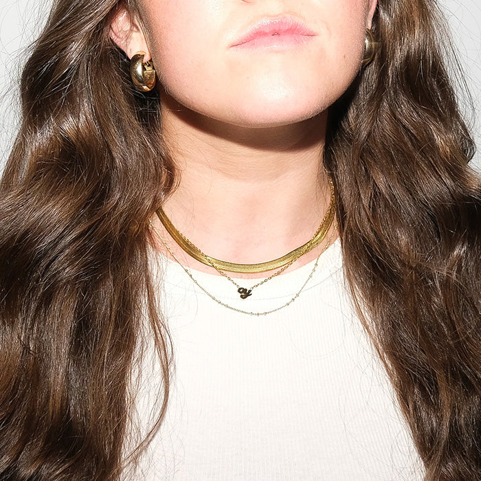 Bright flash photo of young woman with long brown hair wearing gold layered necklaces.