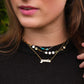 Young woman in black top adjusts her layered necklaces.