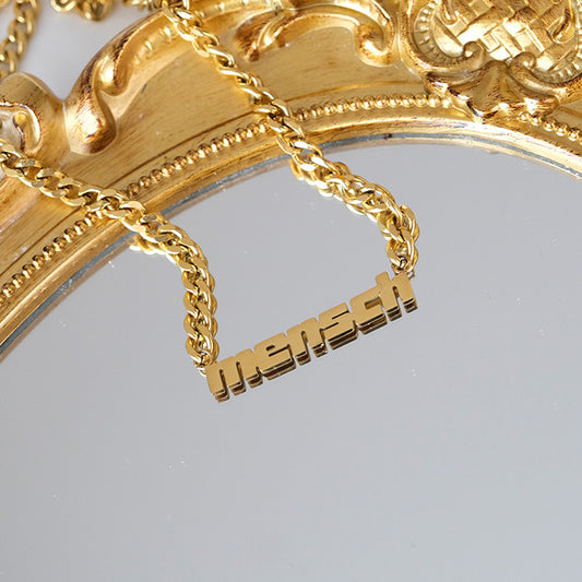 Product shot of gold mensch necklace on gold mirror.