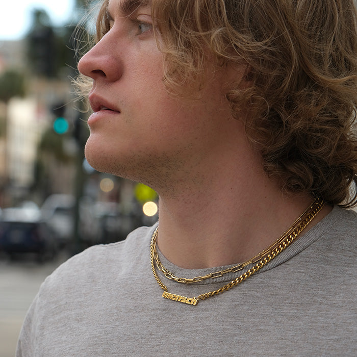 Young man models gold mensch necklace and another chain on gray shirt.